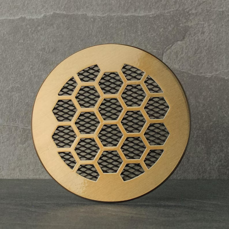 Round brass vent cover with honeycomb pattern on a gray background