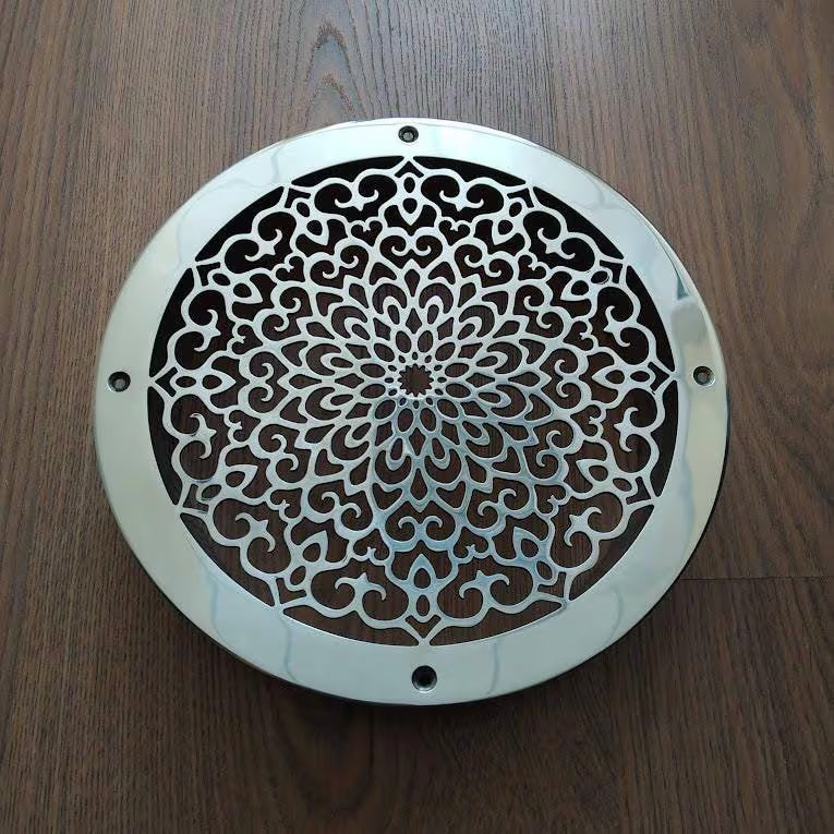 Decorative metal vent cover with intricate patterns on a wooden surface