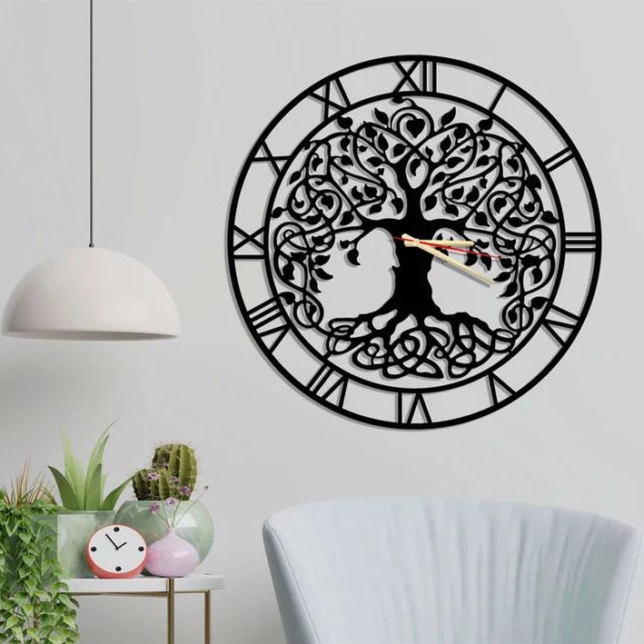 Decorative wall clock with tree design on a white wall, with plants and a chair in the foreground.