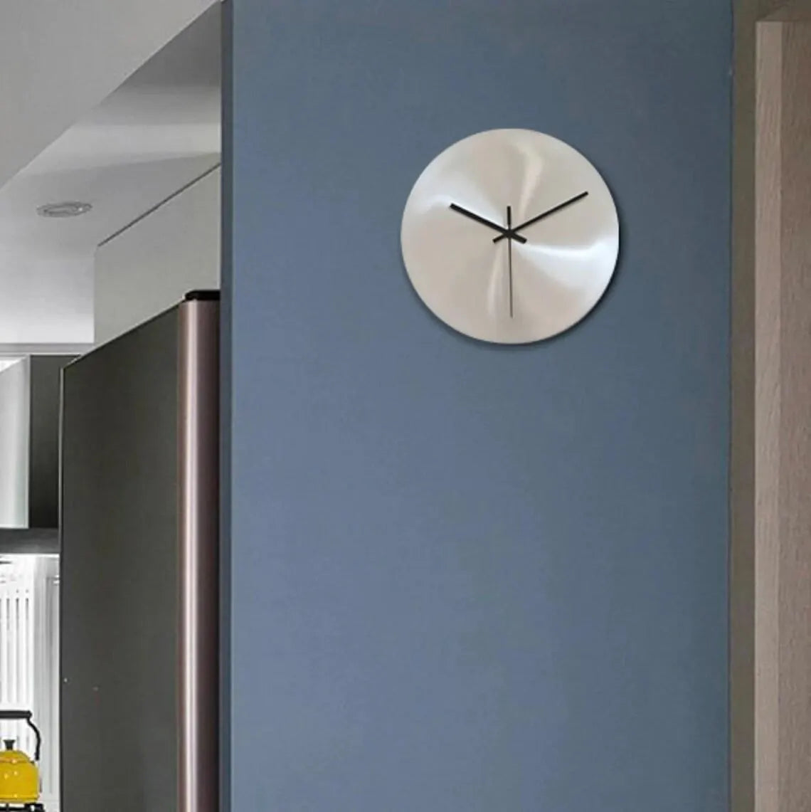 Silver wall clock on a blue wall in a modern interior setting